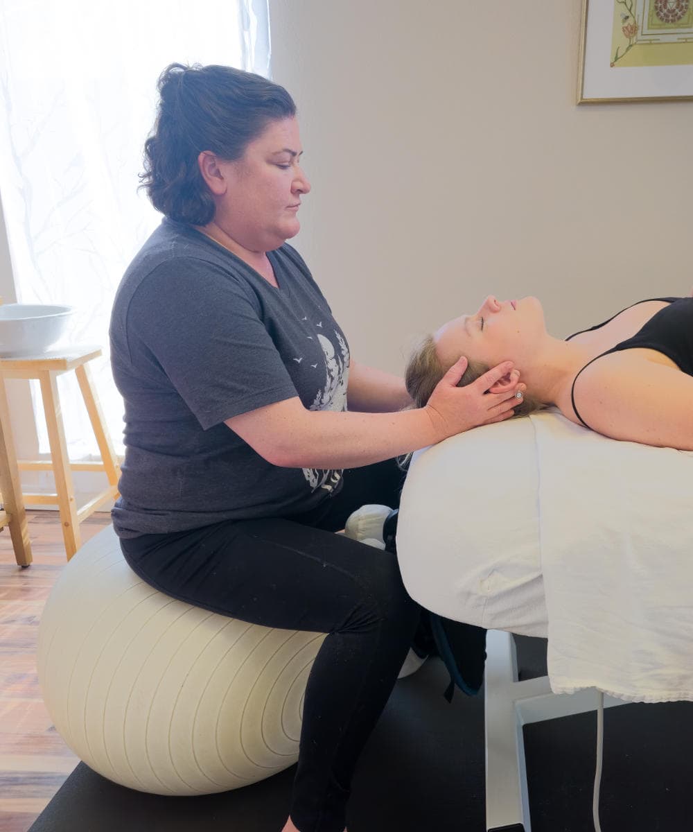 Craniosacral therapist cradles woman's head during session at Whole Being Massage