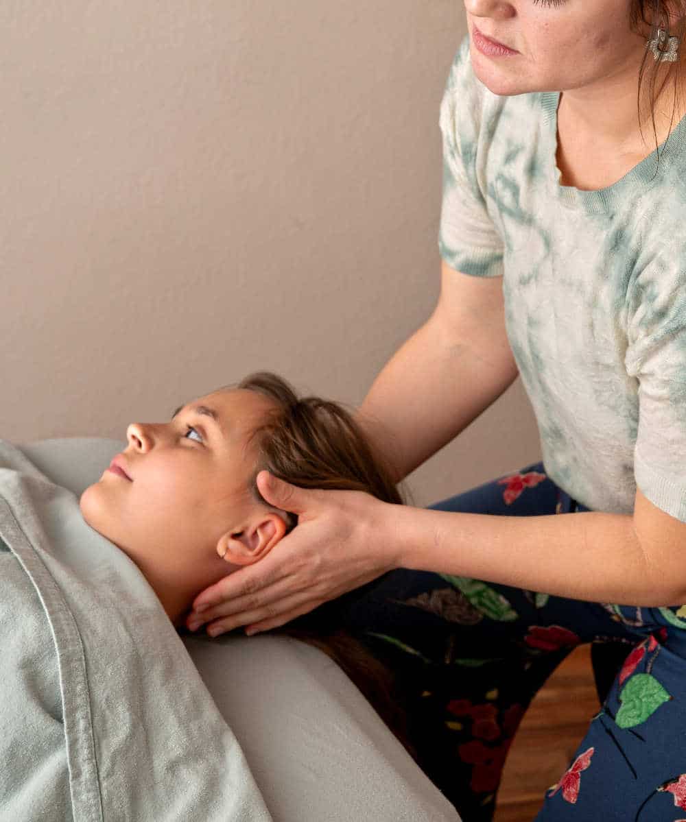 Pediatric massage practitioner cradles a young girls head as she releases tension in neck.