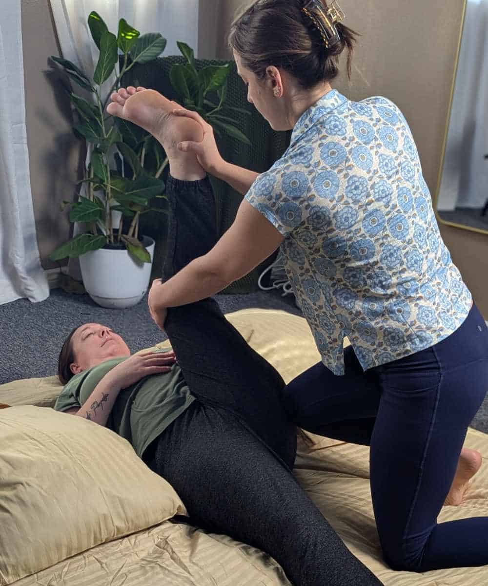 Thai massage therapist uses her knee to apply pressure during a Thai massage for hip pain